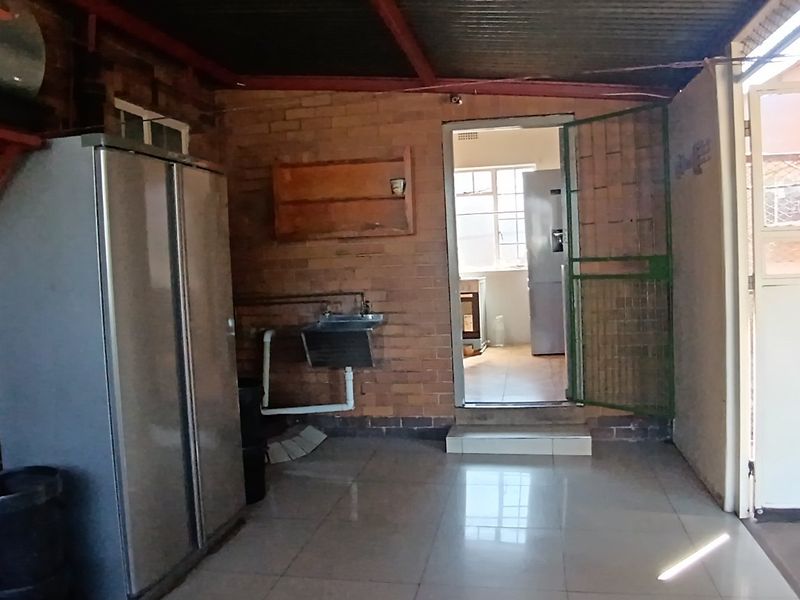 A functional laundry area featuring exposed brick walls, tiled flooring, and a utility sink, with direct access to the main kitchen area.
