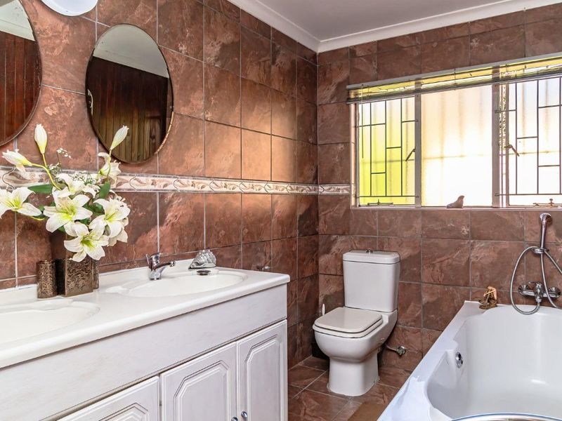 A bathroom featuring a double vanity with built-in cabinetry, a toilet, and a bathtub with tiled wall and floor finishes.
