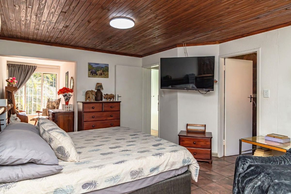 Spacious bedroom featuring a distinctive timber-clad ceiling, tiled flooring, and a wall-mounted air conditioning unit, offering a comfortable and functional living space.