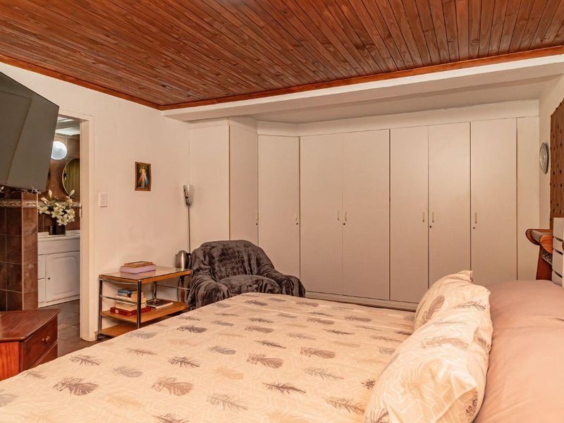 A bedroom featuring a timber-clad ceiling, extensive built-in cupboard storage, and an integrated air conditioning unit, with an adjoining bathroom visible.