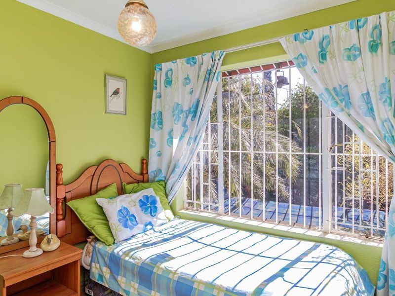 A bedroom featuring green walls, a large window with security bars, and a central ceiling light fixture.