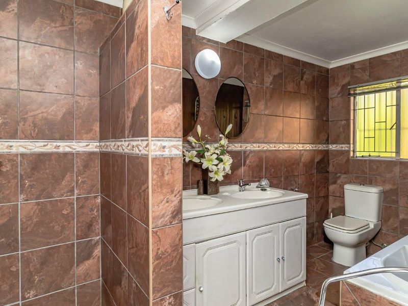 A spacious bathroom featuring a double vanity with built-in cabinetry, a separate shower, a bathtub, and full-height brown wall tiling.