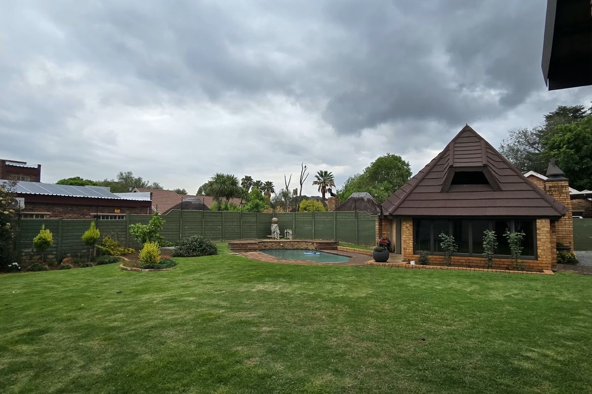 A spacious rear garden featuring a well-maintained lawn, a swimming pool with brick surround, and a detached brick structure with a tiled roof.