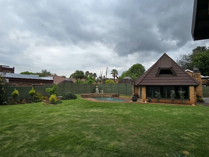 A spacious rear garden featuring a well-maintained lawn, a swimming pool with brick surround, and a detached brick structure with a tiled roof.