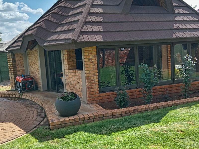 A well-maintained face brick structure with a tiled roof, featuring large aluminium windows and a neat paved area set within a landscaped garden.