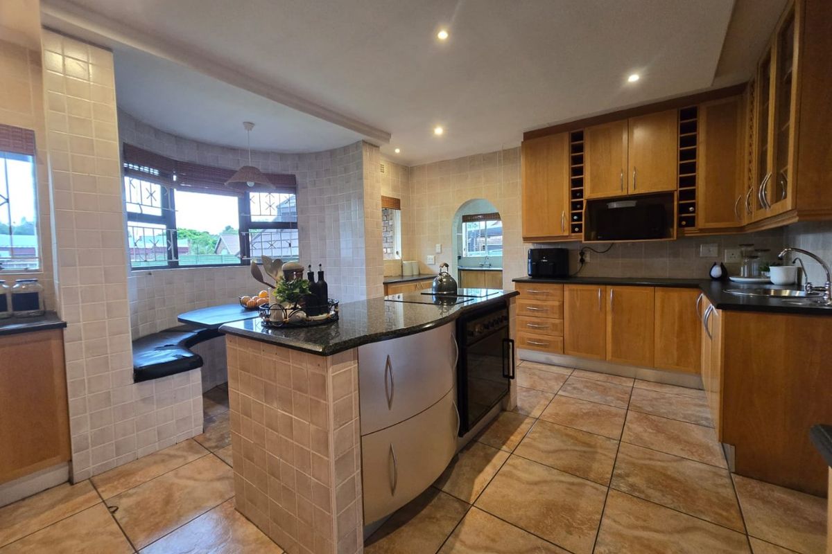 Spacious kitchen featuring wooden cabinetry, granite countertops, a central island with a built-in hob, and a cozy integrated breakfast nook area.
