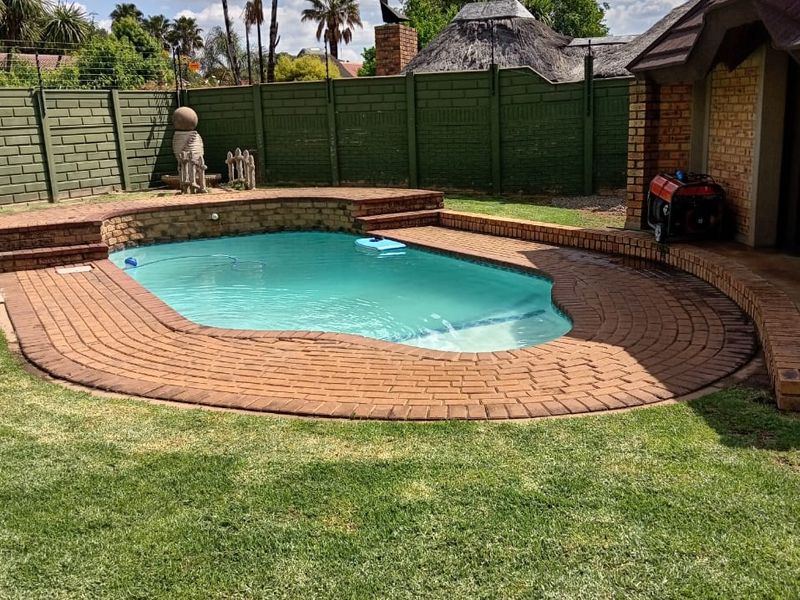 A private backyard featuring a swimming pool with brick surround, a manicured lawn, and a secure perimeter boundary wall.
