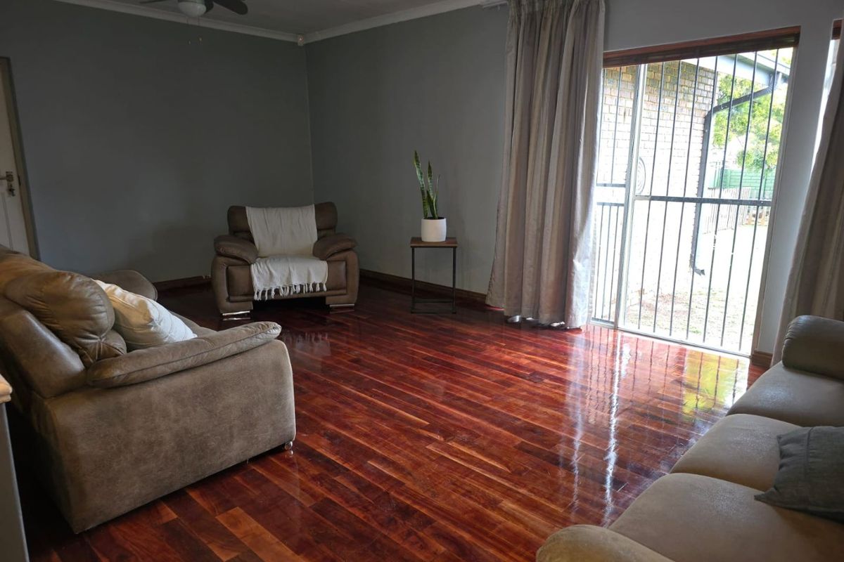 Spacious living room featuring polished hardwood flooring, a ceiling fan, and a sliding glass door with a security gate providing access to the exterior.