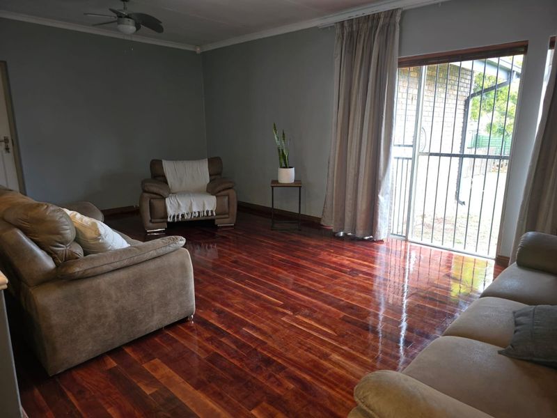 Spacious living room featuring polished hardwood flooring, a ceiling fan, and a sliding glass door with a security gate providing access to the exterior.