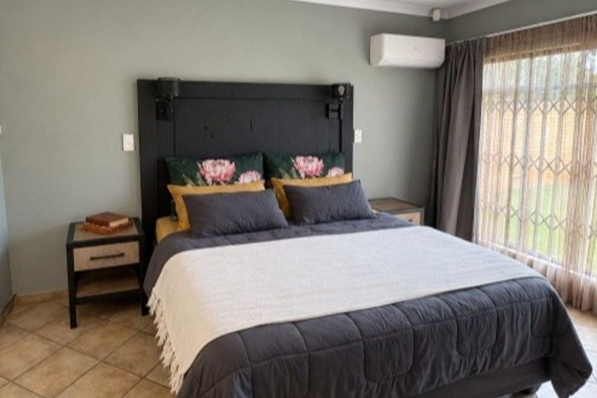 A well-maintained bedroom featuring tiled flooring, a ceiling fan, and a wall-mounted split-system air conditioner for climate control.