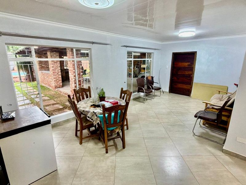Spacious open-plan living and dining area featuring large windows, tiled flooring, and a glossy ceiling, offering direct access to the outdoor patio.