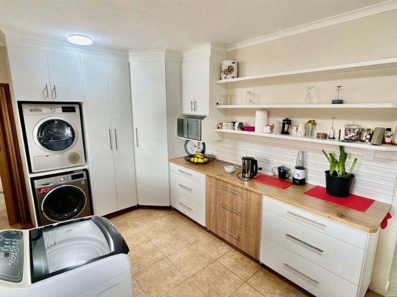 A well-organized laundry room featuring modern white and wood-tone cabinetry, integrated laundry appliances, wooden countertops, and open shelving for storage.