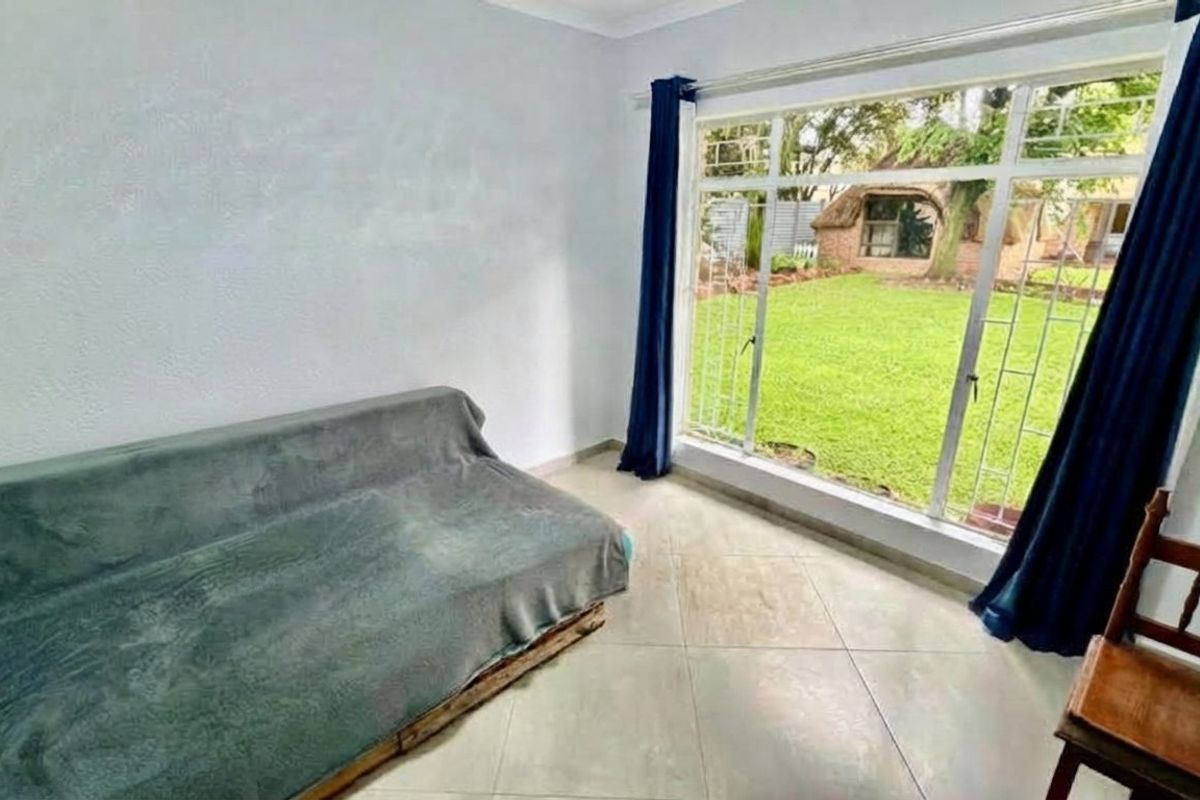 A bright living room featuring large aluminium-framed windows with security bars, tiled flooring, and direct views of the garden.