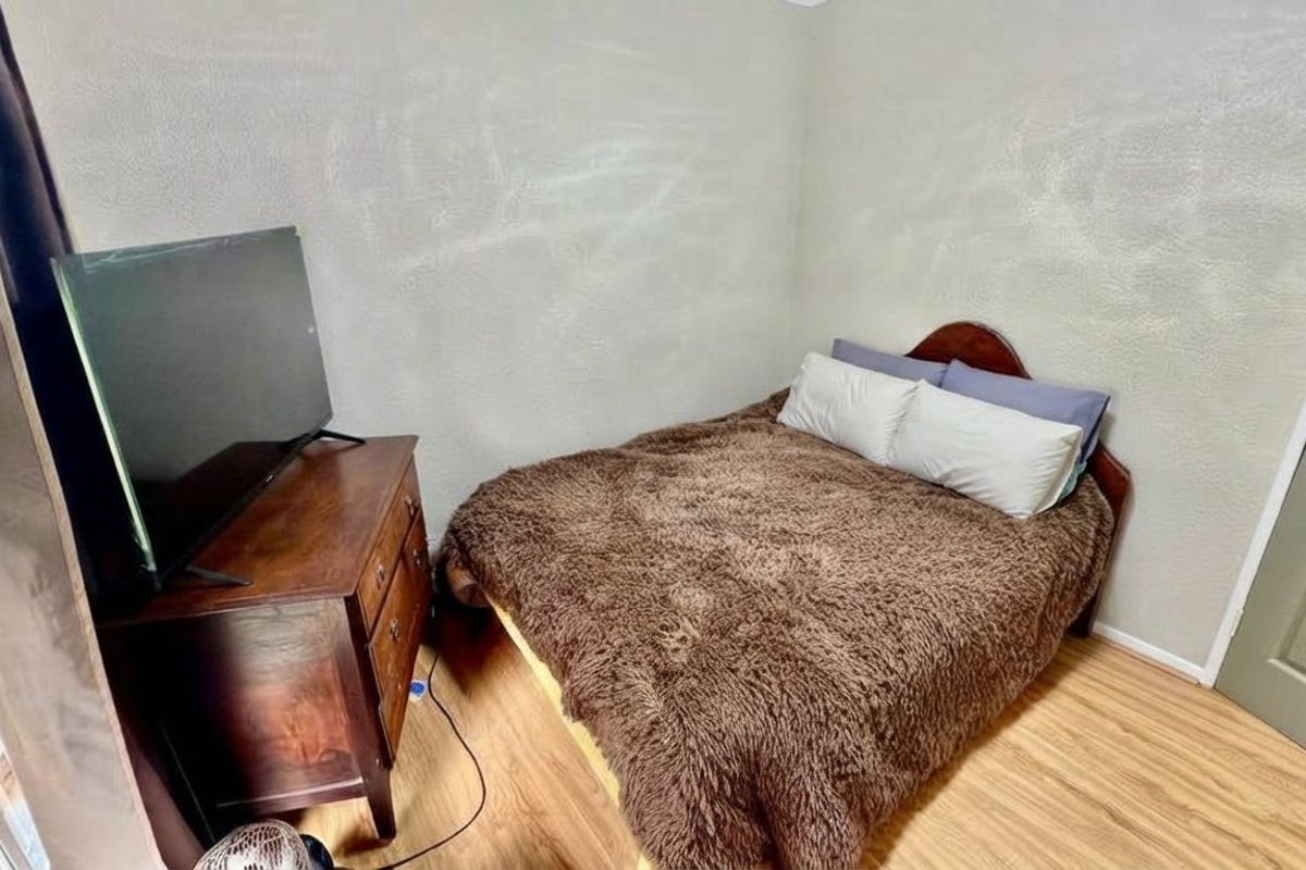 A compact bedroom featuring light-toned laminate flooring and textured walls, offering a functional space ready for cosmetic updates.