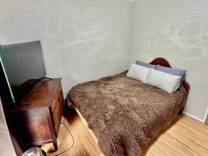 A compact bedroom featuring light-toned laminate flooring and textured walls, offering a functional space ready for cosmetic updates.