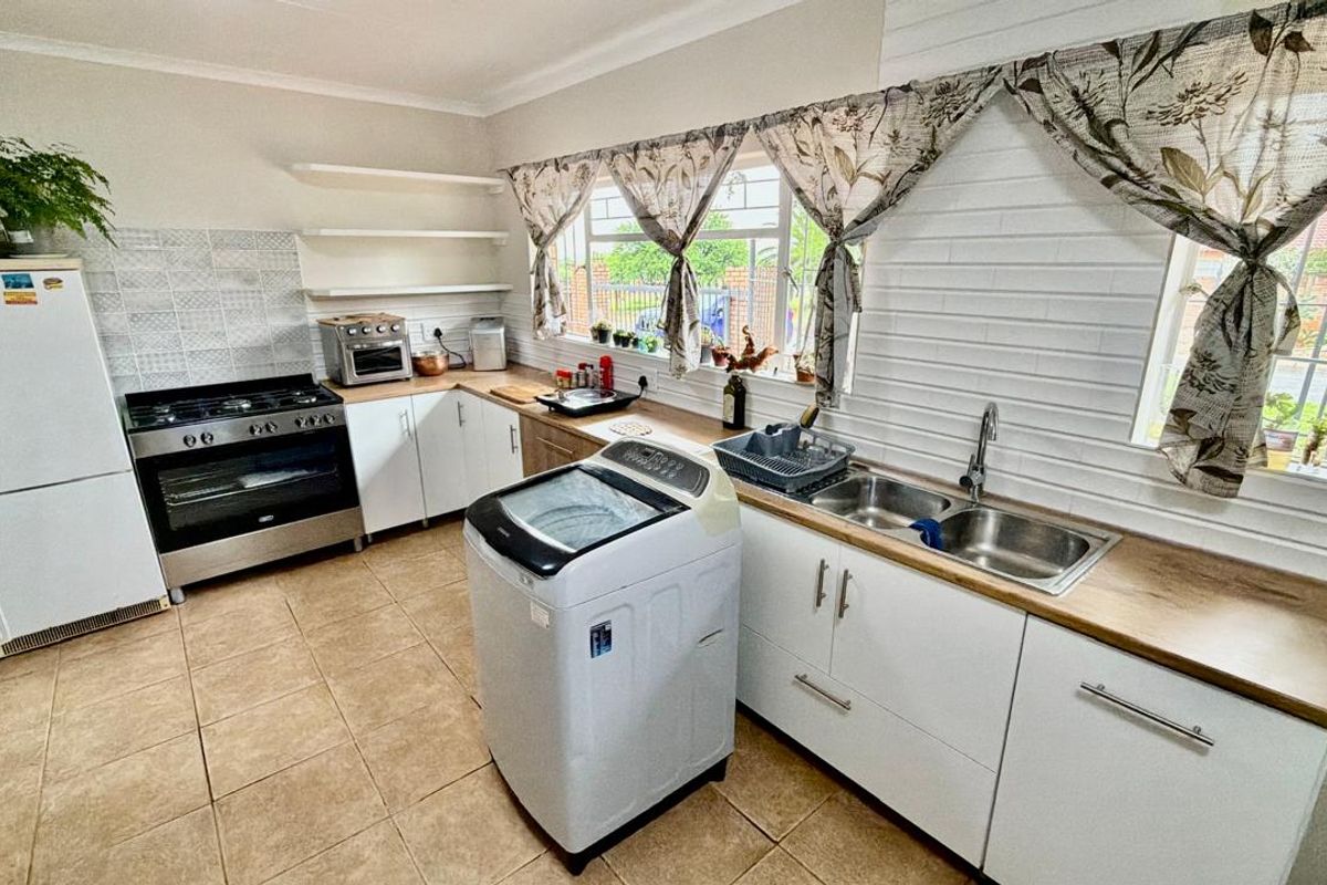 A functional kitchen featuring white cabinetry, timber countertops, a gas stove, and a double basin sink with tiled flooring.