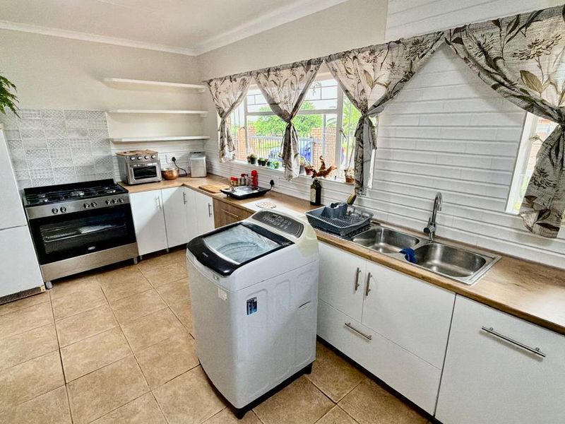 A functional kitchen featuring white cabinetry, timber countertops, a gas stove, and a double basin sink with tiled flooring.