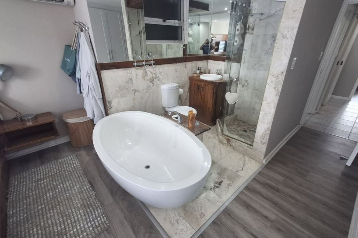 Modern bathroom featuring a freestanding bathtub, glass-enclosed shower, vanity cabinet, and elegant marble-style wall tiling.