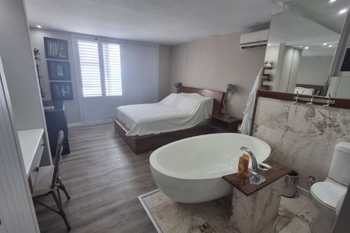 Spacious open-plan bedroom featuring an integrated ensuite area with a freestanding bathtub, marble-look tiling, built-in storage, and air conditioning.