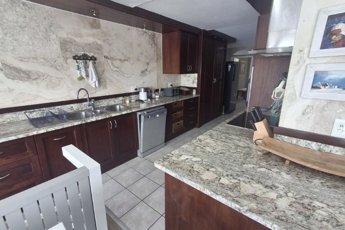 A functional kitchen featuring dark wood cabinetry, granite countertops, stone wall cladding, and integrated appliances, offering a classic aesthetic with potential for modern updates.