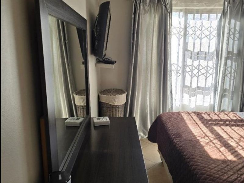 A functional bedroom featuring tiled flooring and a window fitted with a security gate and curtain rails.