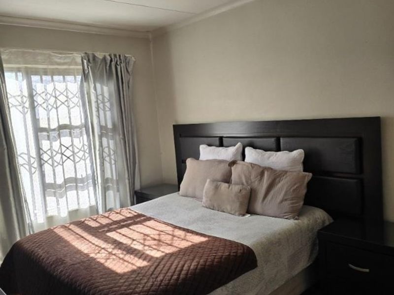 A functional bedroom featuring tiled flooring, a security gate on the window, and a central ceiling light fixture.