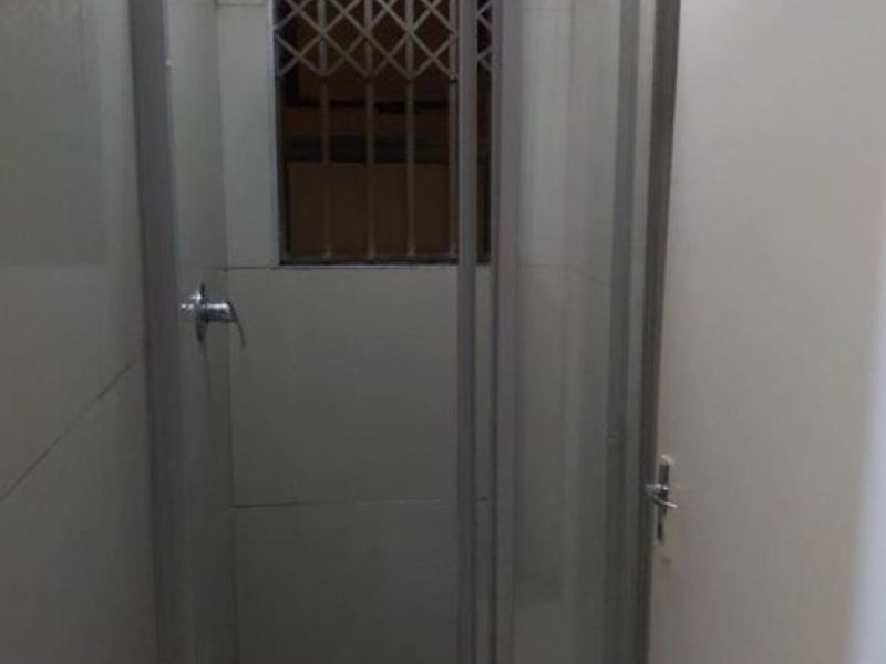 A compact bathroom shower cubicle featuring tiled walls, a glass enclosure, and a window with a security gate.
