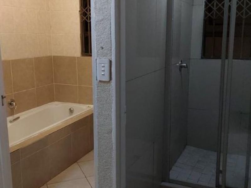 A functional bathroom featuring a separate built-in bathtub and a glass-enclosed shower with neutral wall and floor tiling.