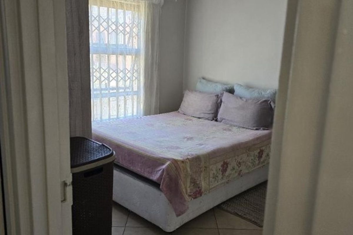 A functional bedroom featuring tiled flooring and a window fitted with a security gate, viewed from the doorway.