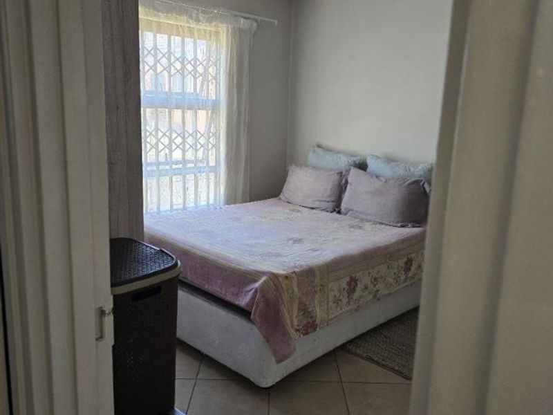 A functional bedroom featuring tiled flooring and a window fitted with a security gate, viewed from the doorway.
