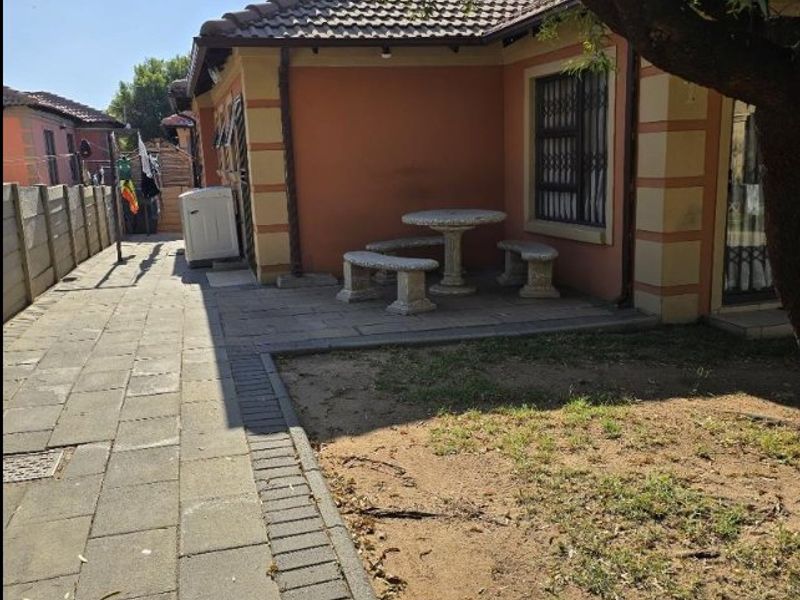 A rear exterior view of the house featuring a paved patio area, security bars on windows, and a surrounding precast concrete boundary wall.