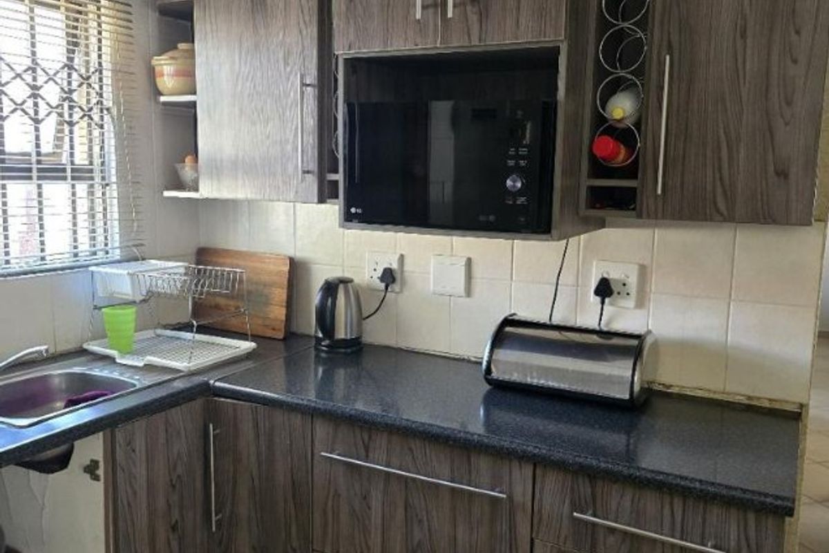 Compact kitchen featuring wood-grain laminate cabinetry, dark countertops, built-in microwave, and tiled backsplash. Requires minor repairs to cabinetry and kickplates.