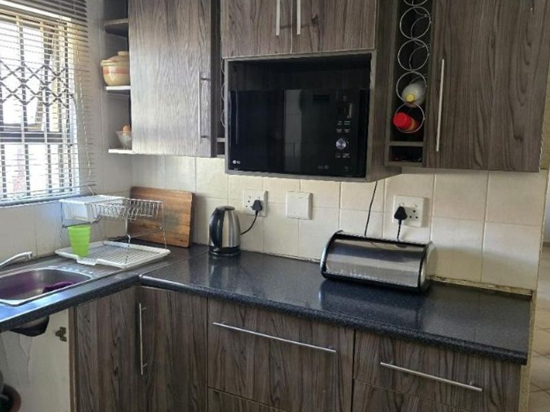Compact kitchen featuring wood-grain laminate cabinetry, dark countertops, built-in microwave, and tiled backsplash. Requires minor repairs to cabinetry and kickplates.
