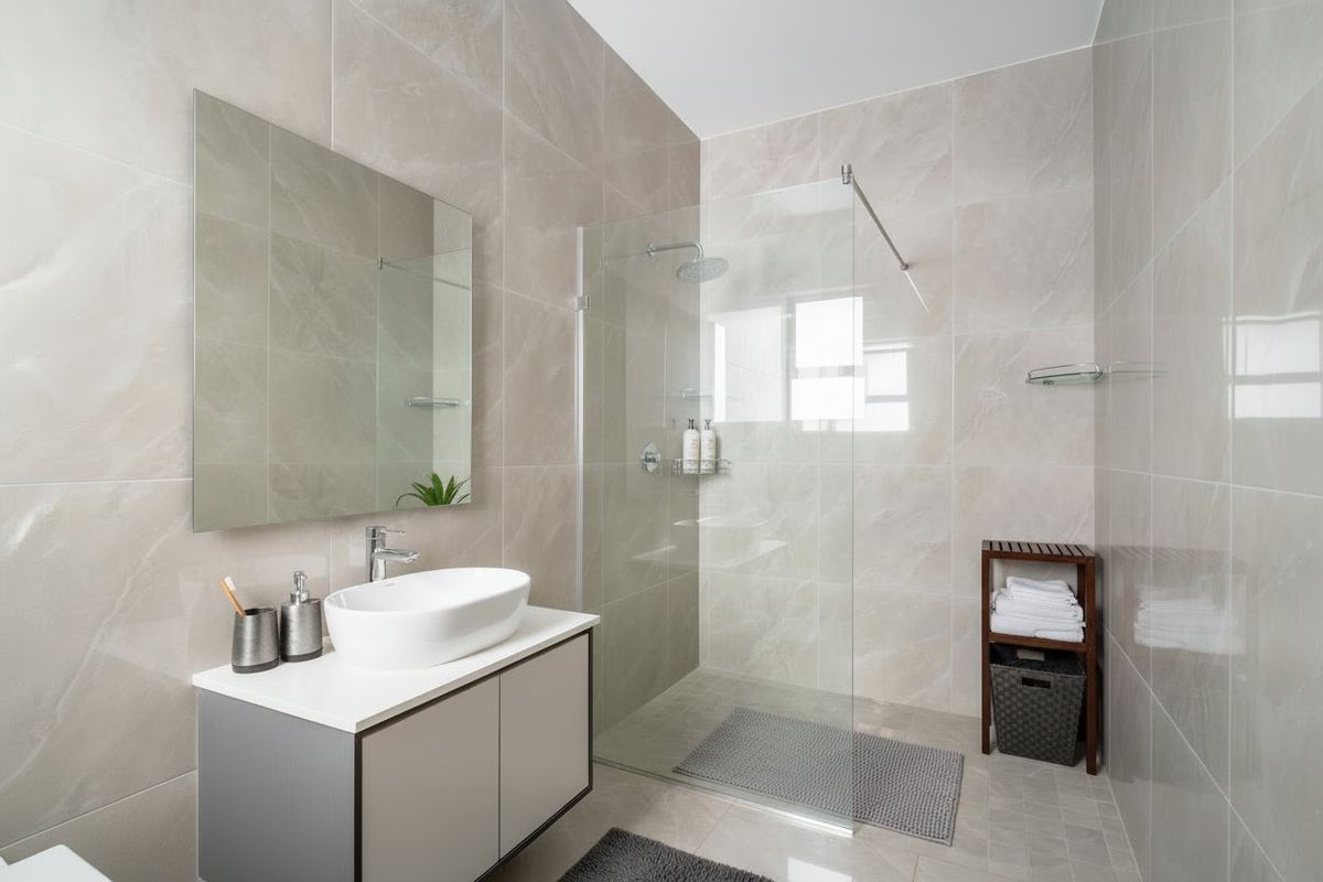 Modern bathroom featuring a sleek vanity with countertop basin, large wall mirror, and a spacious walk-in shower with glass screen and rain shower head.
