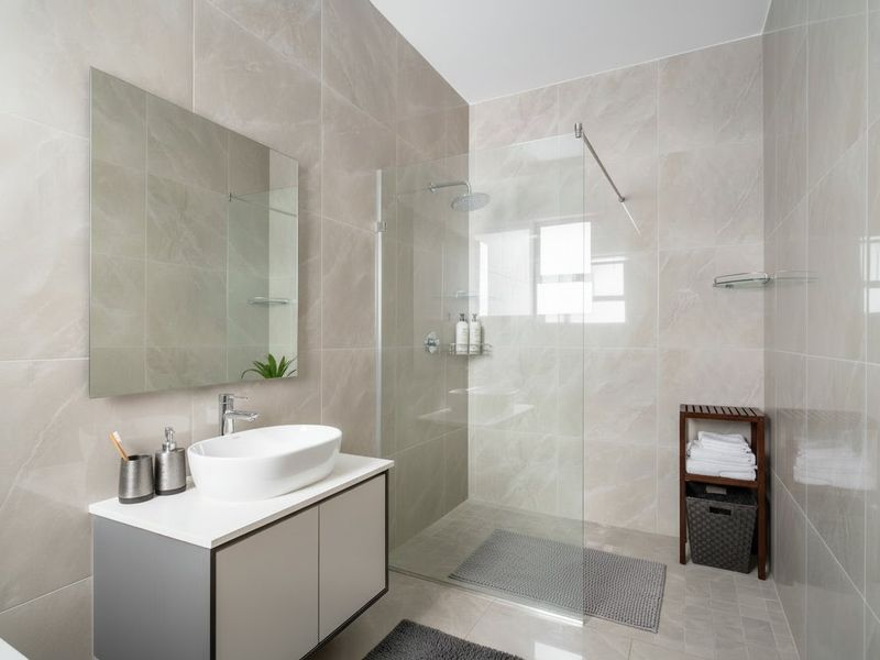 Modern bathroom featuring a sleek vanity with countertop basin, large wall mirror, and a spacious walk-in shower with glass screen and rain shower head.