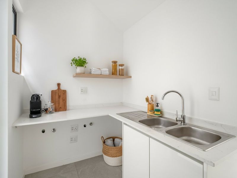 A clean and modern laundry area featuring a double stainless steel sink, stone countertops, and built-in cabinetry with plumbing connections for appliances.