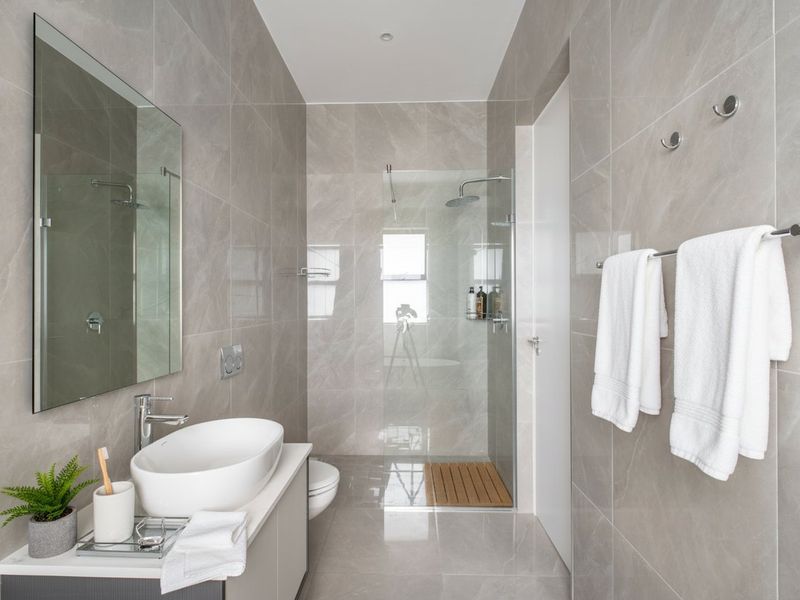 Modern bathroom featuring a floating vanity with vessel sink, glass-enclosed walk-in shower with rain head, and contemporary grey porcelain wall and floor tiling.