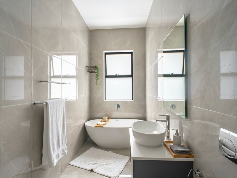 Modern bathroom featuring floor-to-ceiling neutral tiling, a sleek freestanding bathtub, a vessel sink vanity, and a wall-mounted toilet flush system.