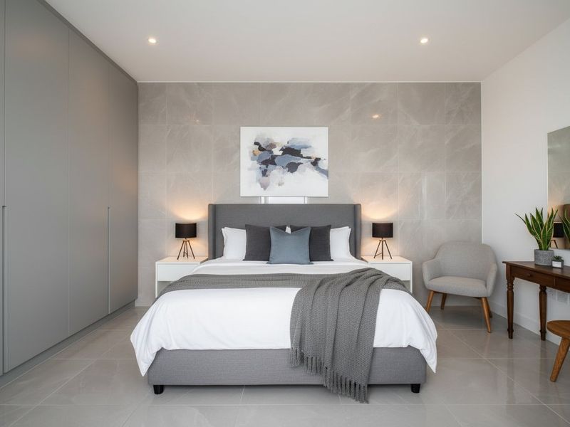 A modern, well-appointed bedroom featuring sleek built-in cupboards, large-format wall tiles, and polished floor tiles with recessed lighting.