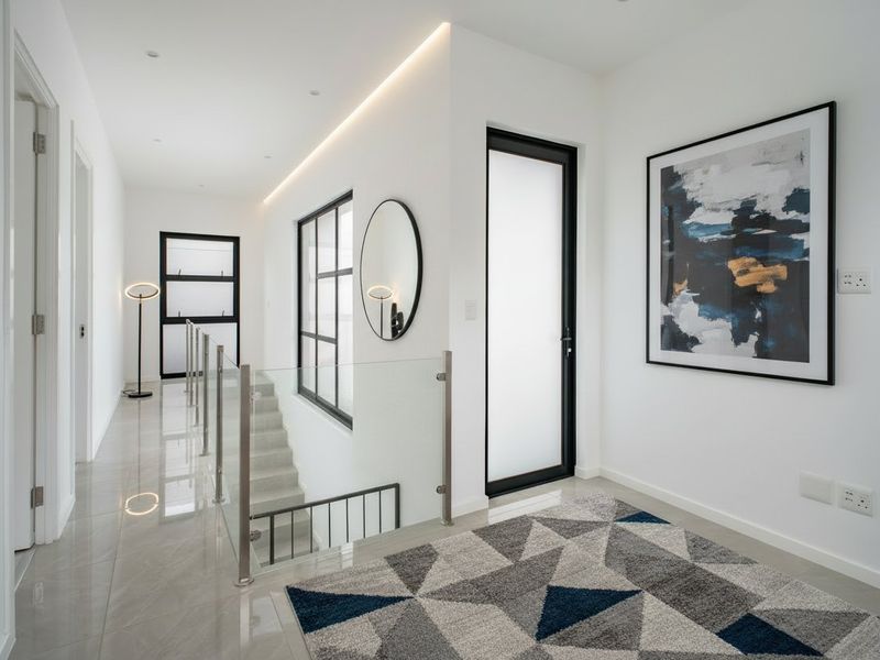 Modern, bright hallway featuring a glass balustrade, sleek tiled flooring, and contemporary black-framed doors with integrated recessed lighting.