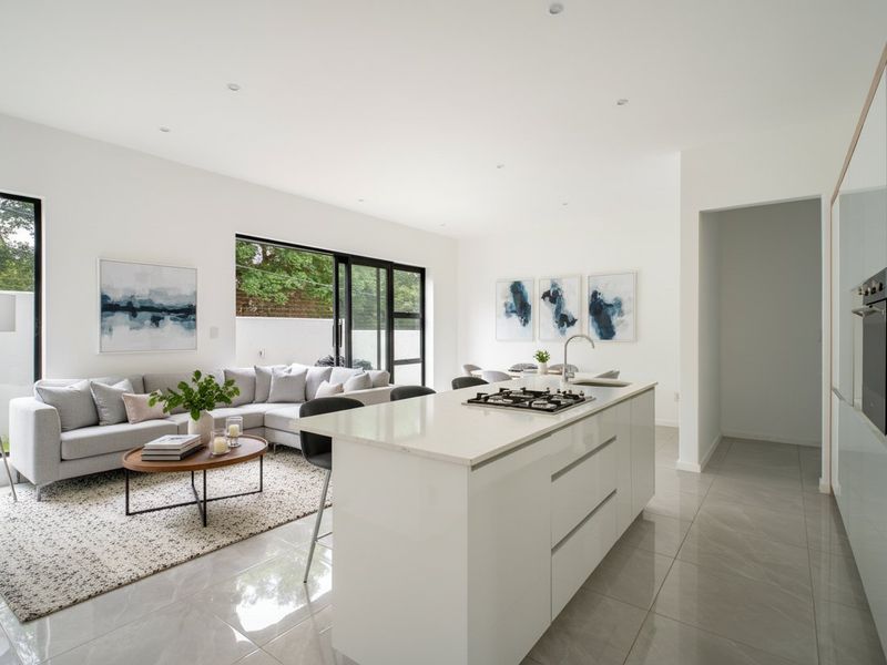 Modern open-plan living area featuring a sleek kitchen island with gas cooktop, integrated cabinetry, and large sliding doors leading to the exterior.