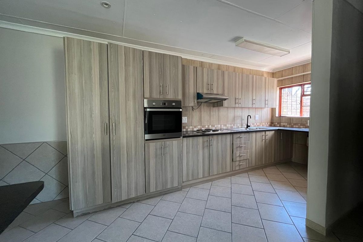 A functional kitchen featuring light wood-grain cabinetry, built-in oven, extractor fan, and tiled flooring with a neutral backsplash.