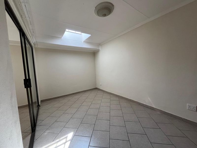 An empty bedroom featuring tiled flooring, a skylight for natural illumination, and a sliding glass door entrance.