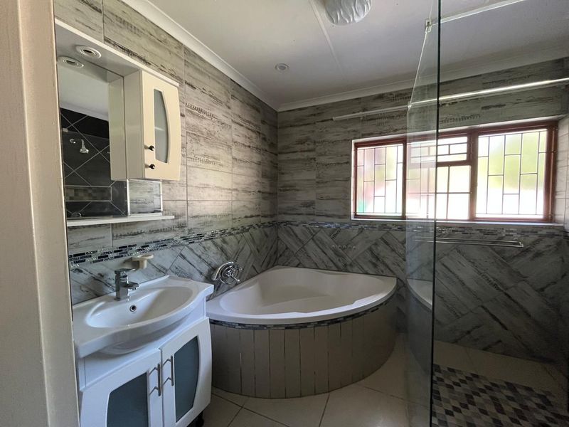 A well-maintained bathroom featuring a corner bathtub, vanity basin, and a glass-enclosed shower area with decorative tiled walls.