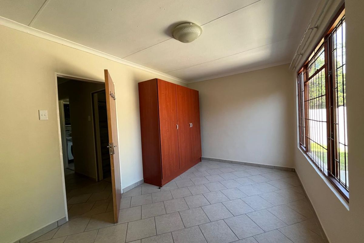 A functional bedroom featuring tiled flooring, a built-in wardrobe, and large windows with security bars, offering a clean and simple living space.