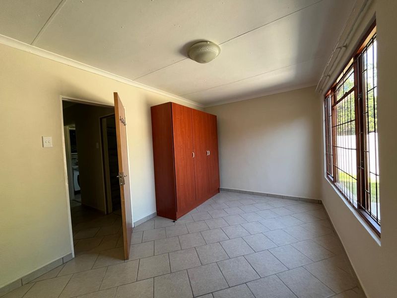 A functional bedroom featuring tiled flooring, a built-in wardrobe, and large windows with security bars, offering a clean and simple living space.