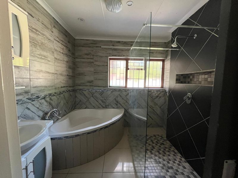 Modern bathroom featuring a corner bathtub, a spacious walk-in shower with a glass screen, and contemporary wall tiling.