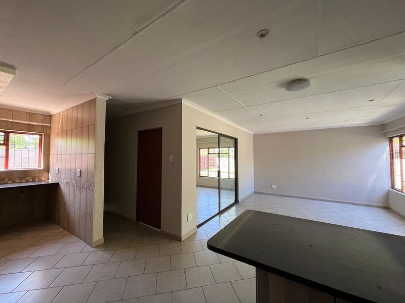 Spacious open-plan living area featuring tiled flooring, a kitchen counter, and sliding glass doors leading to an adjacent room.