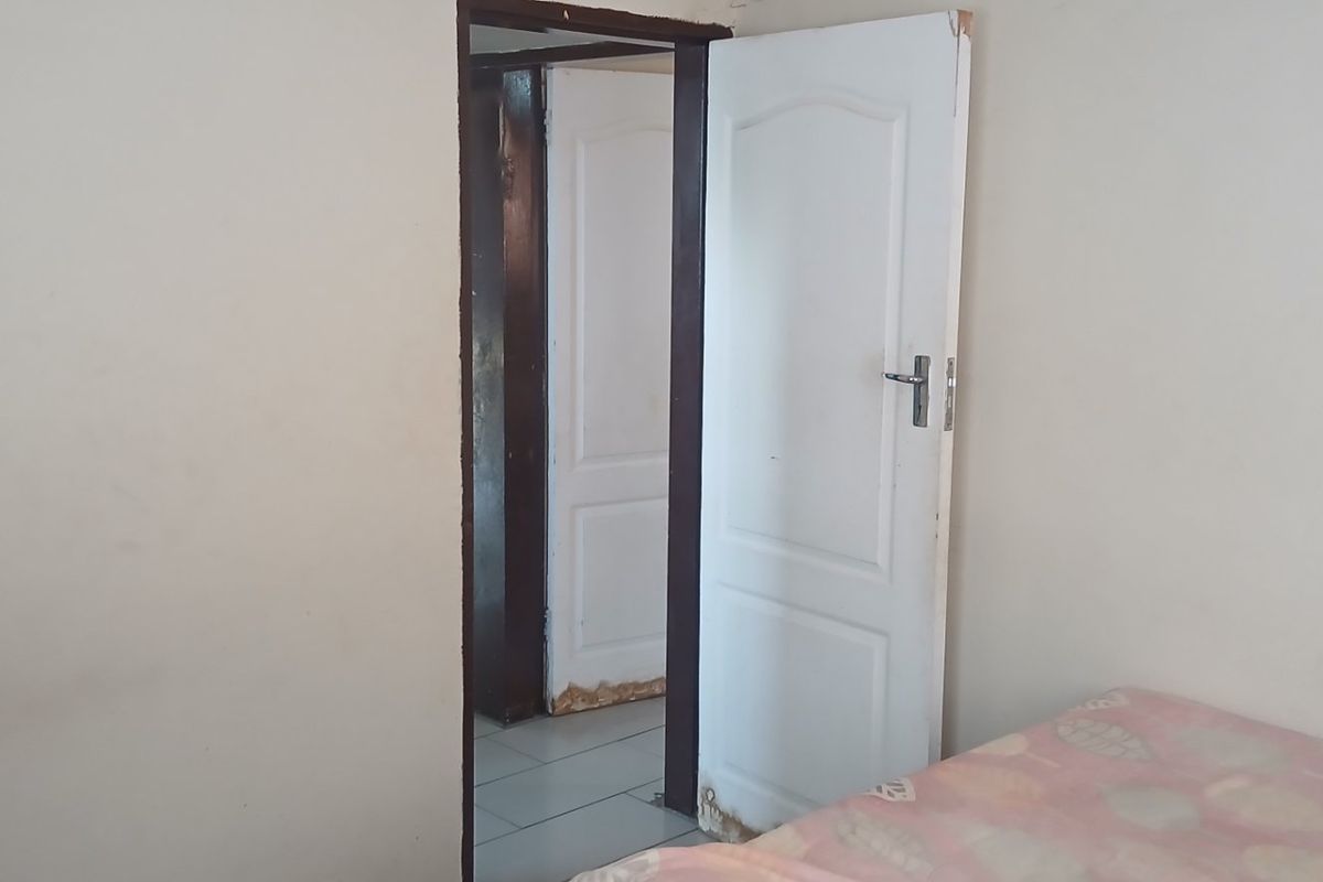 A bedroom interior showing a doorway leading to an adjacent room, featuring visible wear and damage to the door frame finishes.