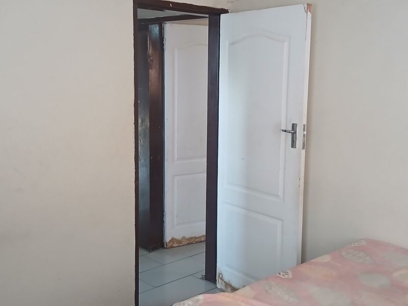 A bedroom interior showing a doorway leading to an adjacent room, featuring visible wear and damage to the door frame finishes.